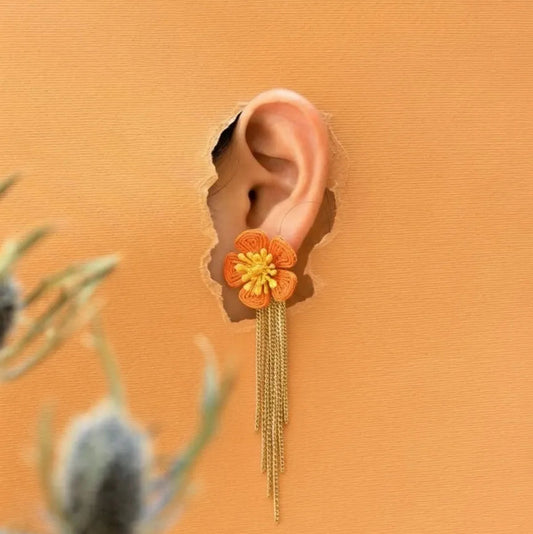 Floral earring with gold chains worn on an ear against an orange background