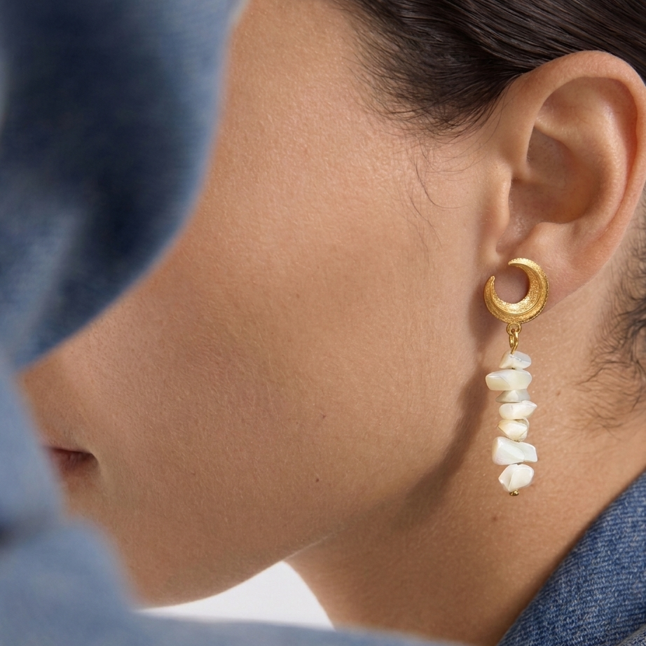 Close-up of a person wearing a gold earring with pearl-like stones.