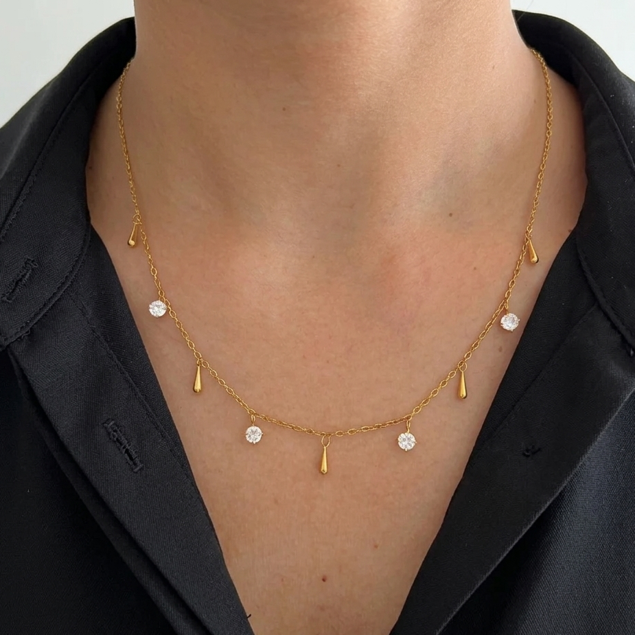 Gold necklace with small pendants on a female wearing a black shirt.