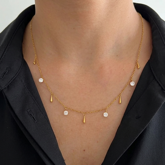 Gold necklace with small pendants on a female wearing a black shirt.