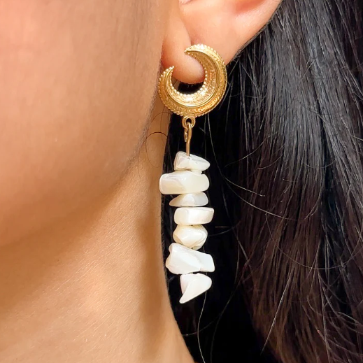 Gold earring with a crescent moon design and pearl-like beads worn by a person.