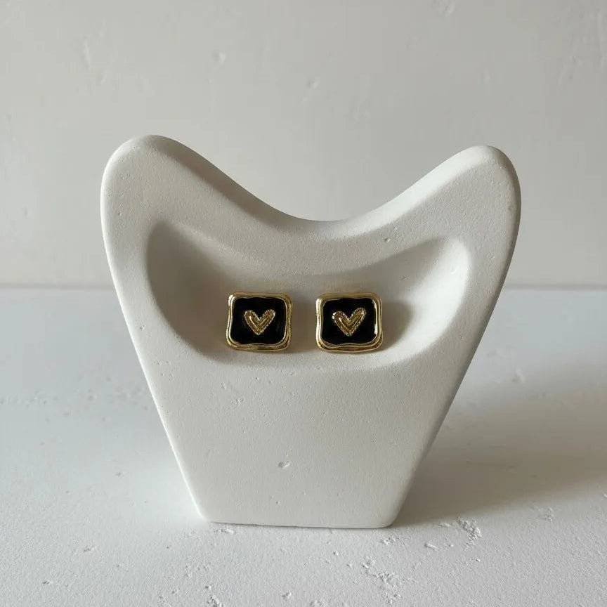 Pair of square earrings with gold hearts on a white stand against a light gray background